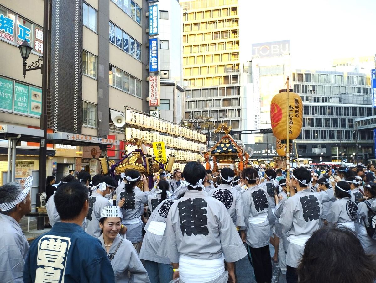 神輿を担ぐ姿の六角精児さん。頭に烏帽子 えぼし をかぶり、白丁 はくちょう と呼ばれる白装束で身を包む。提供：ヴァンブック - 調布経済新聞